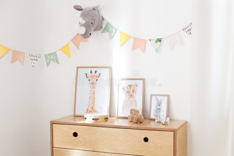 Simple posters, photo frames, wooden eco toys placed on a wooden chest of drawers stood in white interior of the children room wit royalty free stock photography