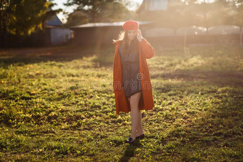 Sixteen-year-old smiling teen girl in a red beret and orange coat in direct sunlight outdoors royalty free stock photo