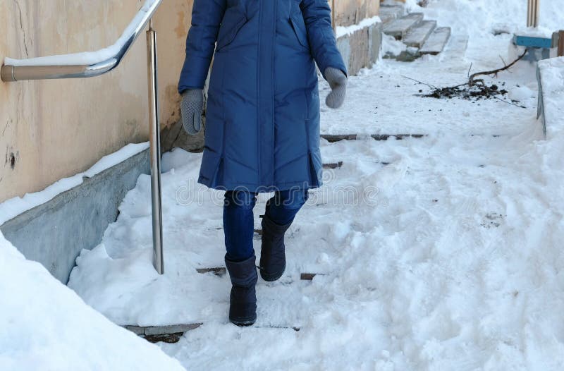 Slippery stairs. Unrecognizable woman in a blue down jacket walking down a snowy staircase. Slippery stairs. Unrecognizable woman in a blue down jacket walking royalty free stock photos