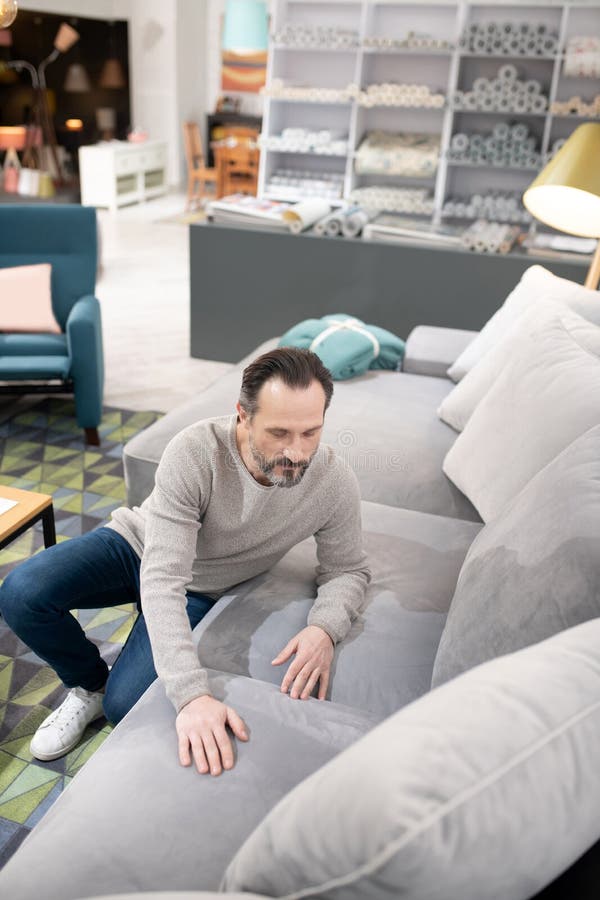 Man in light sweater and jeans touching the sofa. Soft and smooth. Man in light sweater and jeans touching the sofa stock image