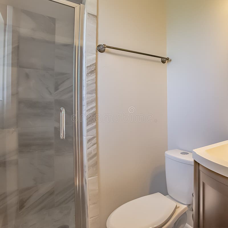 Square frame Bathroom interior of a home with toilet sink and cabinet against the white wall. Mirror with lights are mounted above the sink and the shower stock photography