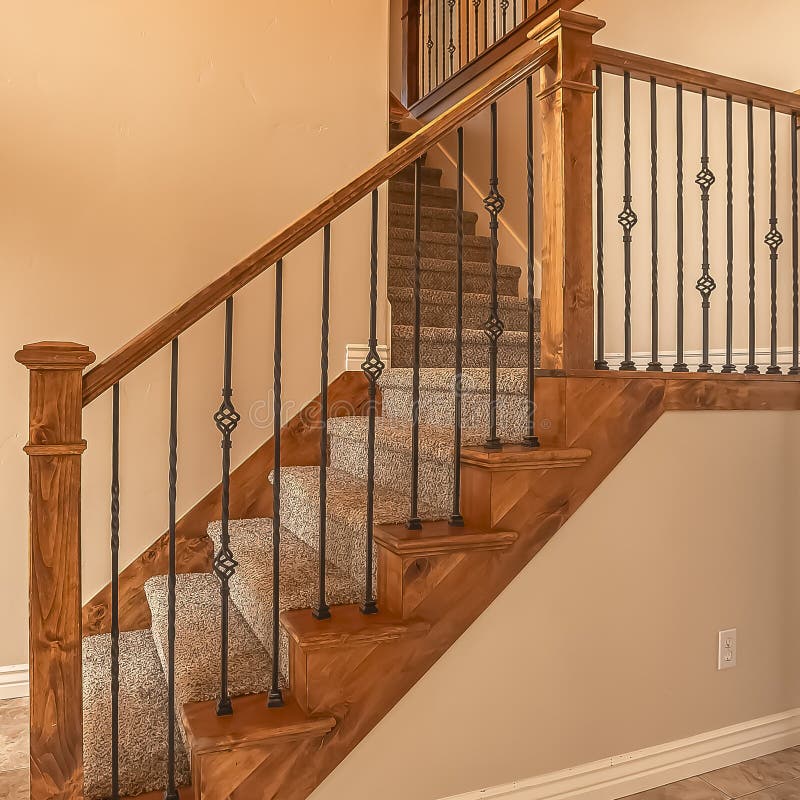 Square frame Carpeted stairs with wood handrail and metal railing inside an empty new home. Beige wall, shiny floor, window with blinds, and arched doorway can stock photography