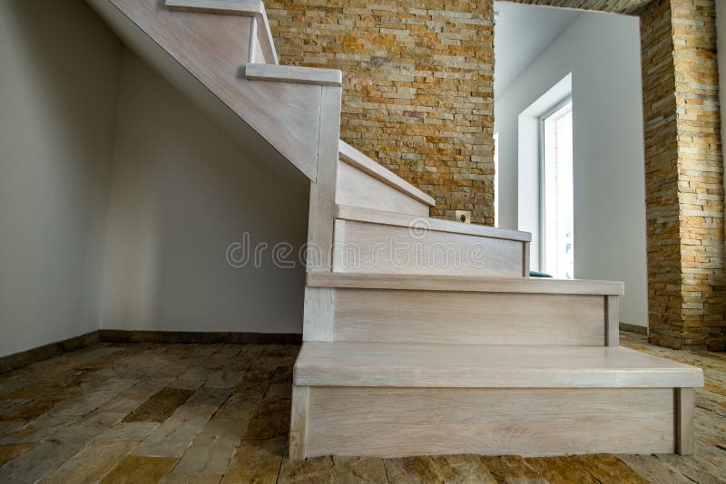 Stylish wooden contemporary staircase inside loft house interior. Modern hallway with decorative limestone brick walls and white stock image