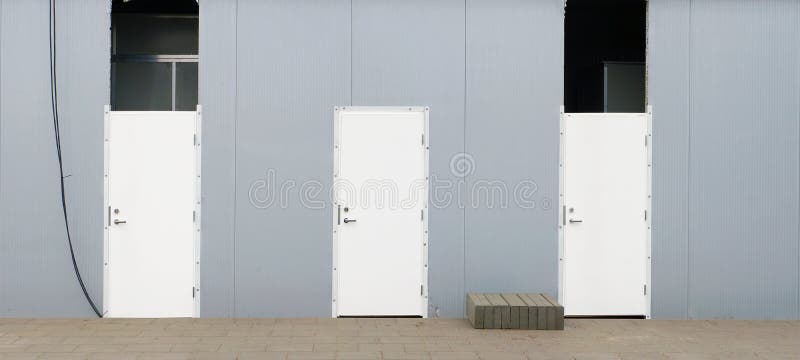 Three new white armored doors in the steel wall of an urban unfinished shopping center royalty free stock image