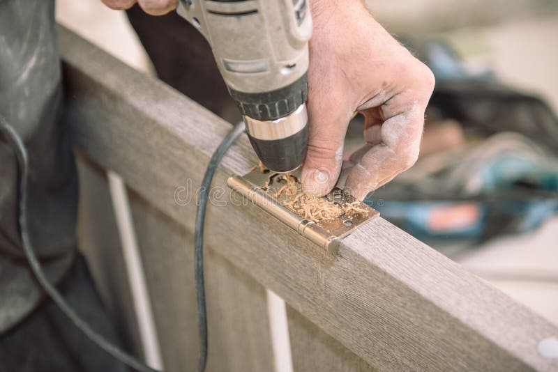 To fasten the hinge. The man fastens the hinge. Twist the hinges on the door. Installation of door hinges. Door installation. Tighten the screws on the door stock photography