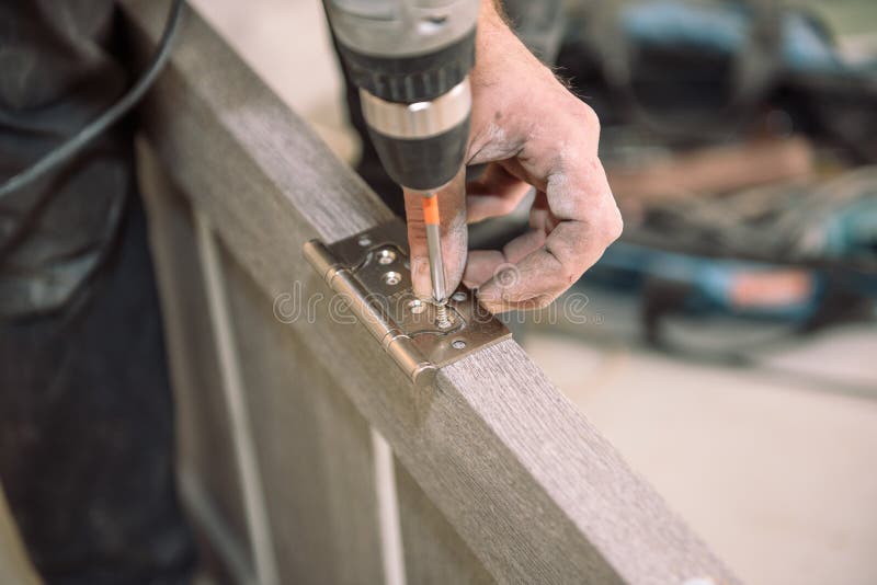 To fasten the hinge. The man fastens the hinge. Twist the hinges on the door. Installation of door hinges. Door installation. Tighten the screws on the door stock photography