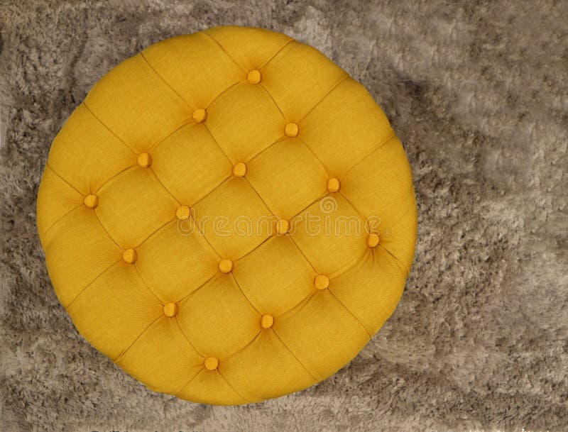 Top view of round fabric yellow pouf with buttons and squares. Gray carpet background.  royalty free stock photography