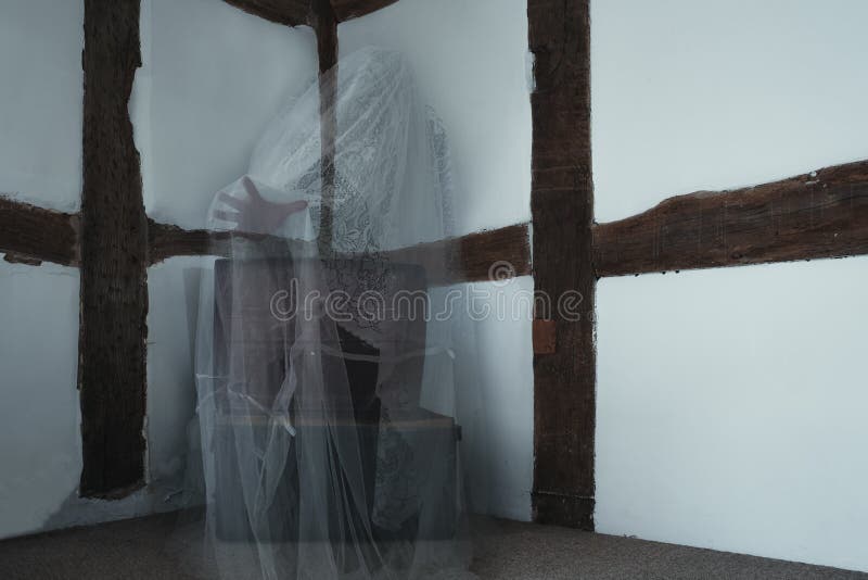A transparent ghost floating above a metal box, hand out stretched, in a corner of an old timber framed building.  stock photo