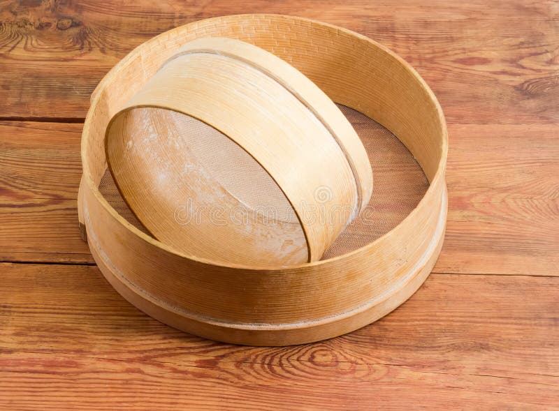 Two old wooden sieves different sizes on old wooden table. Two old round sieves different sizes with wooden frames and plastic mesh on an old rustic wooden stock image