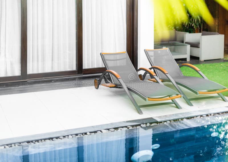 Luxury hotel room with pool, lawn and two sunbeds. Two sunbeds on white floor and windows with curtains behind. Green lawn, Table and armchair in background stock image