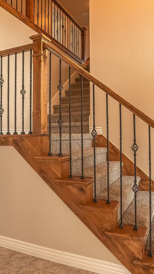 Vertical frame Carpeted stairs with wood handrail and metal railing inside an empty new home. Beige wall, shiny floor, window with blinds, and arched doorway stock photos