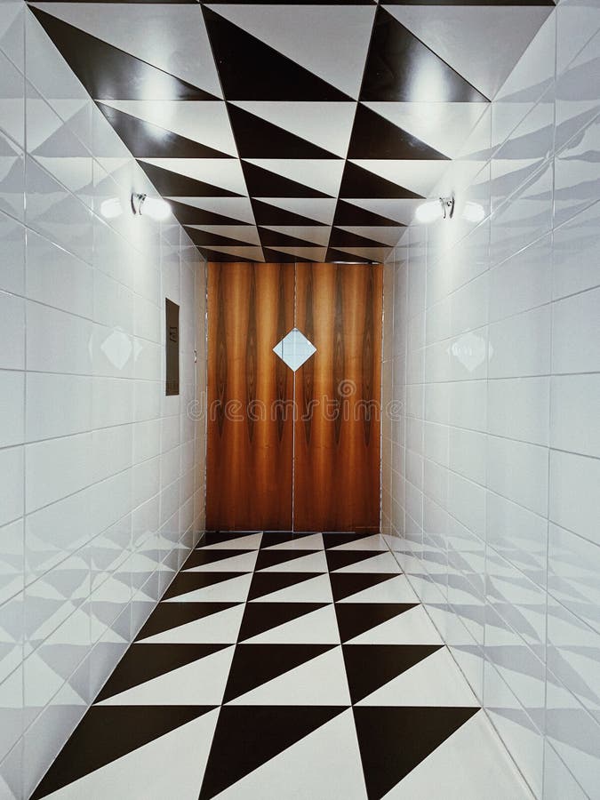 Vertical shot of a well-lighted tiled corridor with wooden door with rhombus window. A vertical shot of a well-lighted tiled corridor with wooden door with stock images