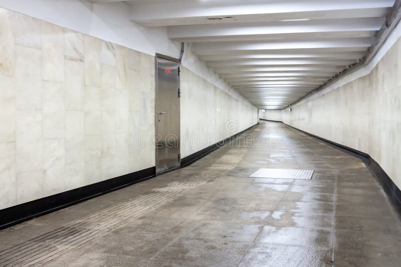 A view down a damp tiled block and concrete tunnel urban or city pedestrian underpass corridor with white wall and. A view down a damp marble tiled block and stock photo