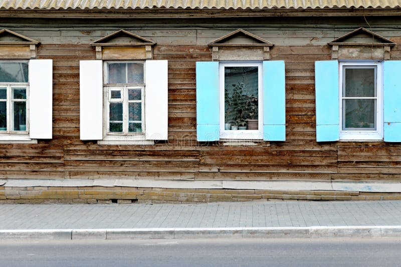 Wall of the aged wooden hut in Astrakhan, Russia. Wall of the aged wooden hut and fragment of pavement in Astrakhan, Russia. Four old vintage windows in royalty free stock image