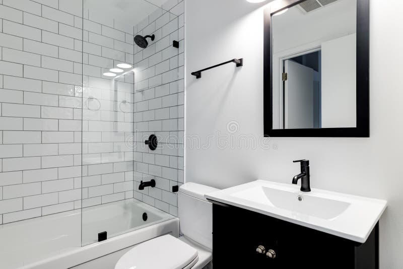 A white bathroom with a dark vanity and black hardware. CHICAGO, IL, USA - DECEMBER 27, 2019: A small modern bathroom with a dark vanity, mirror frame, and royalty free stock photos