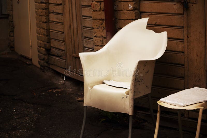 White broken plastic armchair on wooden wall with doors backgrund stock image