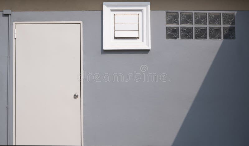 White door, square ventilation shutter and glass blocks with sunlight and shade on surface of gray cement wall royalty free stock photos