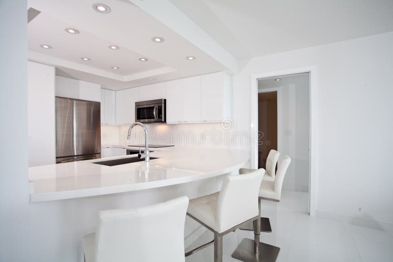 White Kitchen with bar counter. All white kitchen with attached white counter tops, bar, and stools stock image
