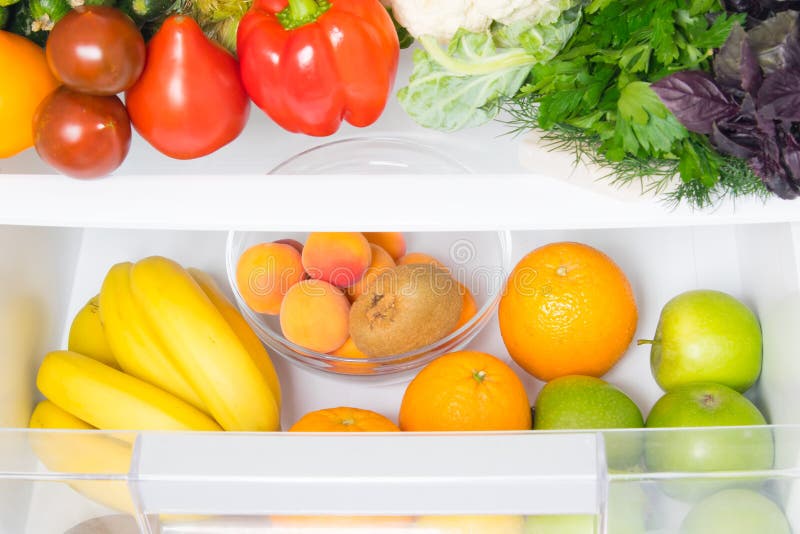 In a white refrigerator, food stock, fresh vegetables on the top shelf, and fruits on the bottom shelf royalty free stock images