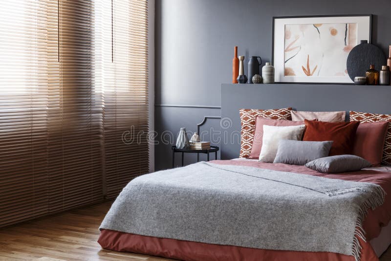 Window blinds in a bedroom interior with a king size bed, cushions, painting and vases stock images