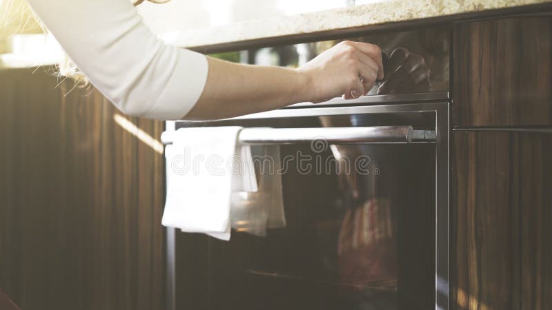 A woman adjusts temperature on the kitchen oven. A woman dressed in white adjusts temperature on the kitchen oven. A woman puts high temperature to bake, cook in royalty free stock photo