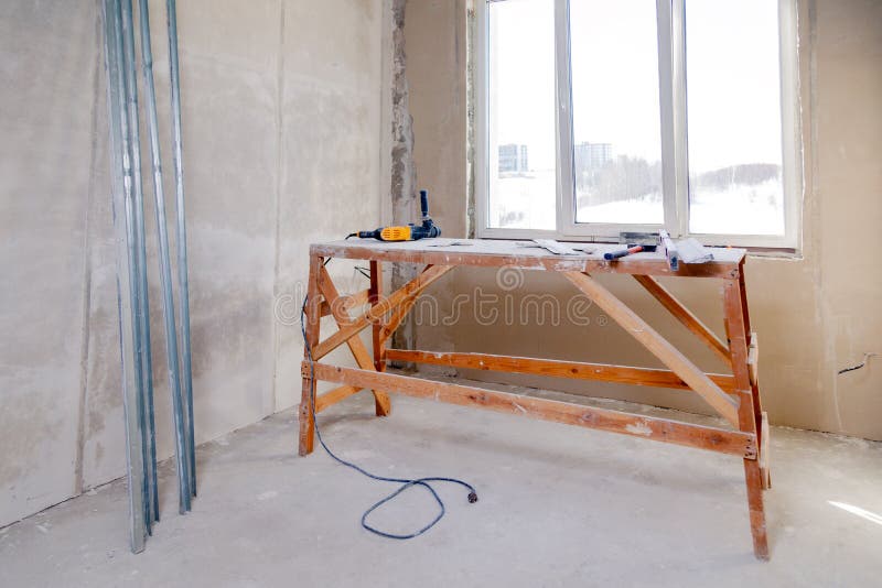 Wooden scaffolding stand at the window in a large empty room, repair, plastering, painting walls, building tools, trash. Concept stock photo