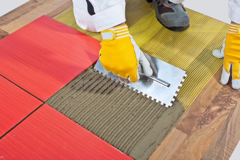 Worker apply ceramic tiles. On wooden floor mesh trowel royalty free stock image