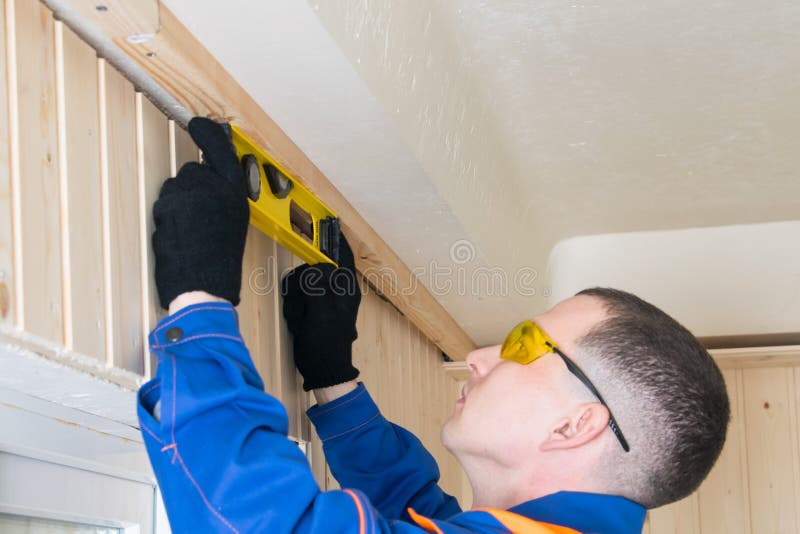 A worker in a blue uniform measures the level of the wooden ceiling log royalty free stock image
