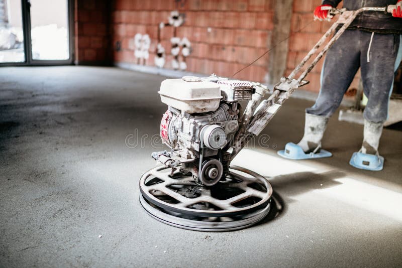 Worker with power trowel tool finishing concrete floor, screed, smooth concrete surface. Industrial Worker with power trowel tool finishing concrete floor stock photo