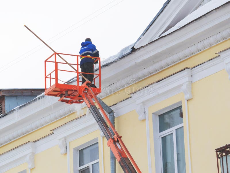 Worker removes snow and ice from the roof of the building stock photo