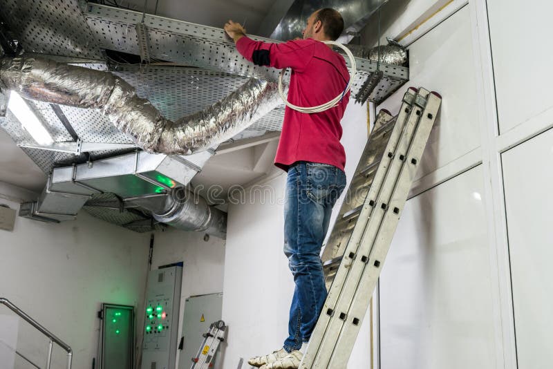 A worker standing on the stairs repairs the ventilation in the technical room of the residential complex. The installer works royalty free stock photos