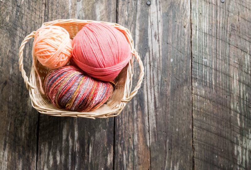 Yarn in worven basket; old wood planks background. Three balls of peach, pink and multicolored yarn in woven basket. Wood grain background. Ideal for copy text stock images