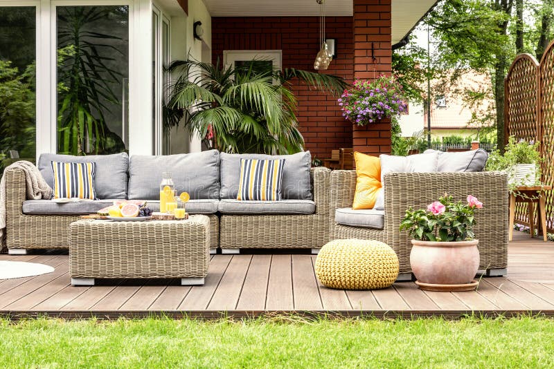 Yellow pouf and flowers next to rattan garden furniture on wooden terrace of house. Real photo. Yellow pouf and flowers next to rattan garden furniture on wooden stock images