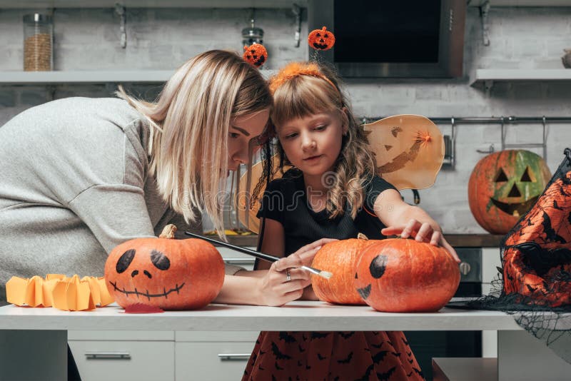 Young woman and little sister painting pumpkins for halloween together in kitchen. At home stock photo