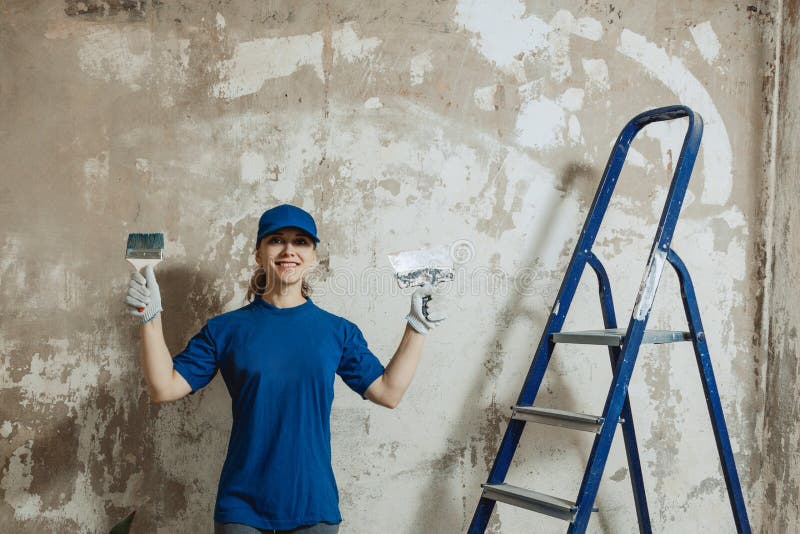 A young woman prepared to do repairs, smiling while standing on the background of a painted wall, royalty free stock images