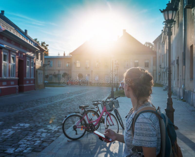 Young woman with a smartphone in her hands on the street in a European city, vintage building and parked bicycles. Bicycle rental. In the city concept stock images